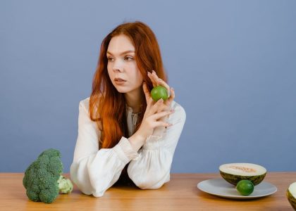 Caucasian woman sitting at table holding lime with broccoli and melon.